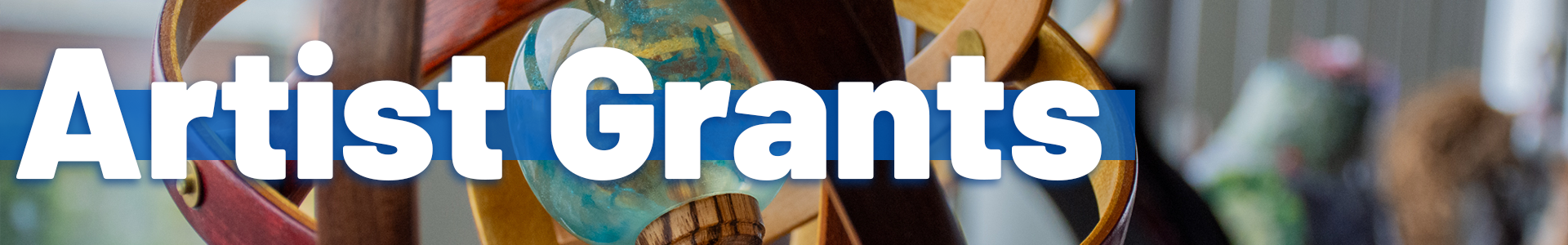 A close-up of a colorful wooden and glass sculpture, with large white text reading ‘Artist Grants’ across a blue bar.