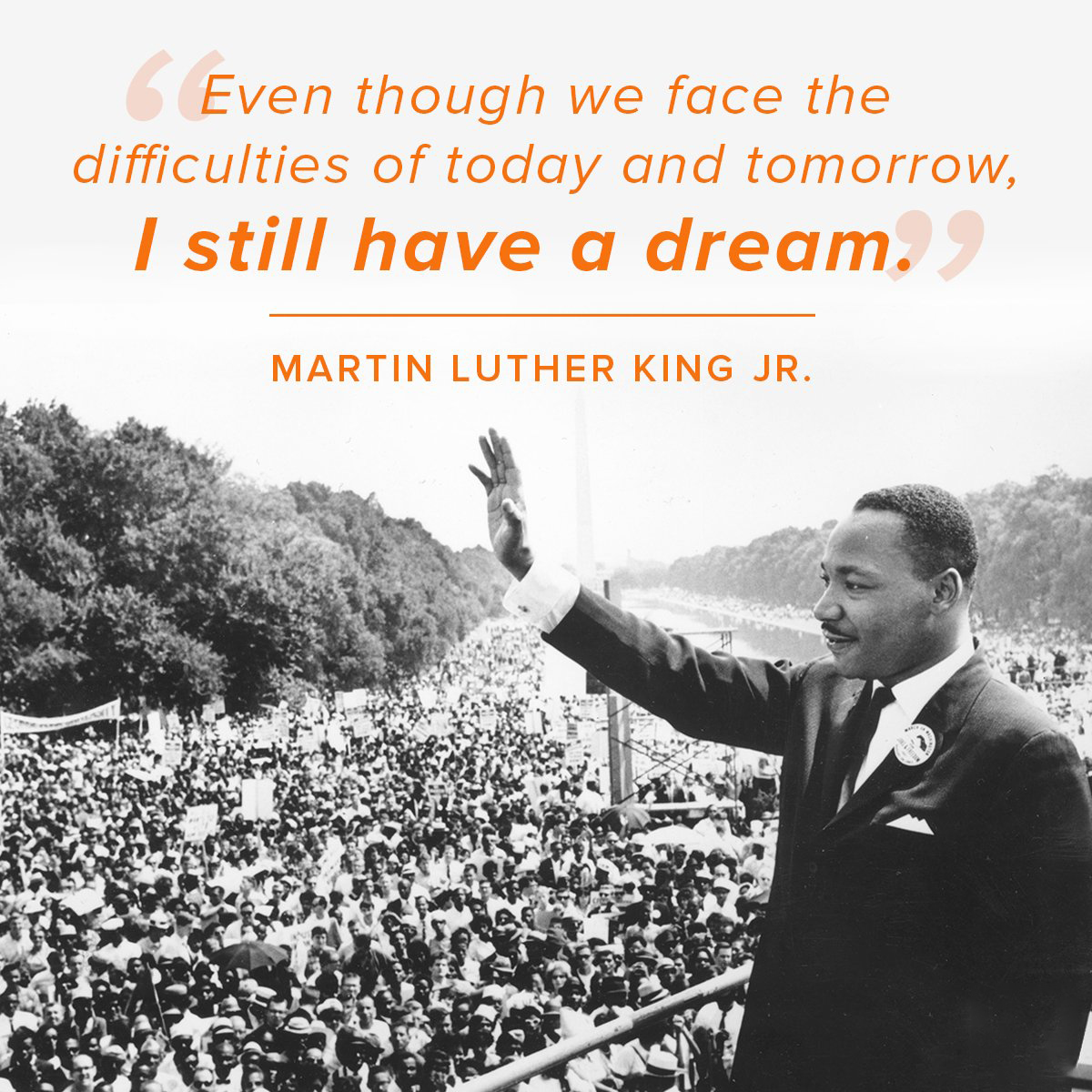 Black-and-white photo of Martin Luther King Jr. standing at a podium and waving to a large crowd gathered along the National Mall. Above him is an orange quote that reads, ‘Even though we face the difficulties of today and tomorrow, I still have a dream.’ The quote is attributed to Martin Luther King Jr