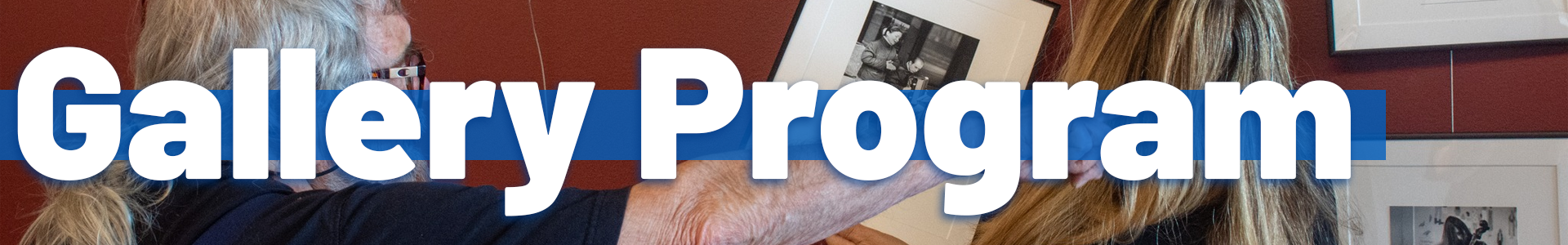 A person with long gray hair adjusts a framed black-and-white photograph on a gallery wall while another person watches. Large white text reading ‘Gallery Program’ appears across the center over a blue bar.