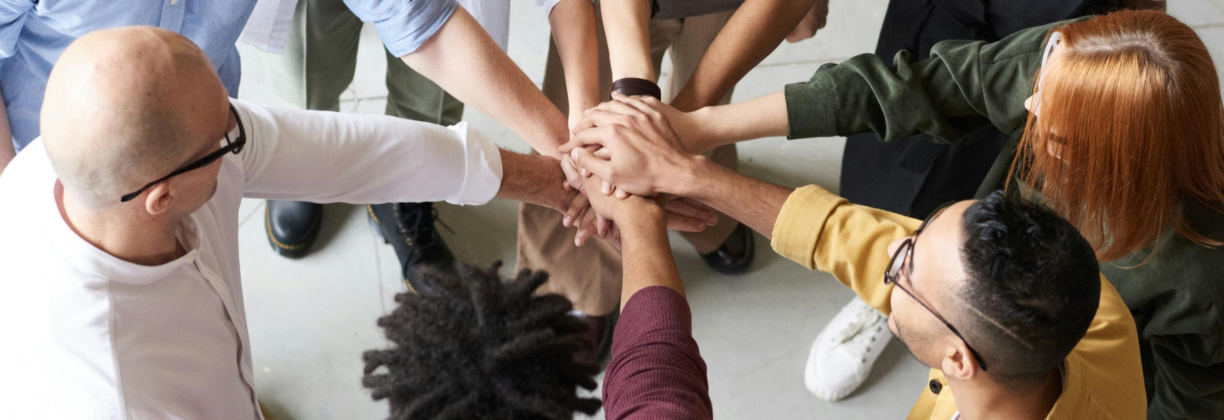 diverse individuals standing in circle with hands touching in the middle