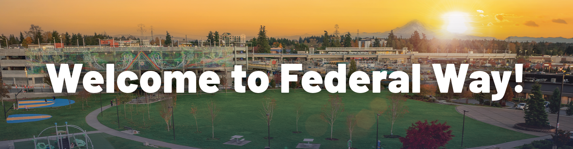 Aerial view of Town Square Park in Federal Way at sunset, showing green open space, walking paths, playground areas, surrounding buildings, and Mount Rainier in the distance. Large white text across the image reads, “Welcome to Federal Way!”