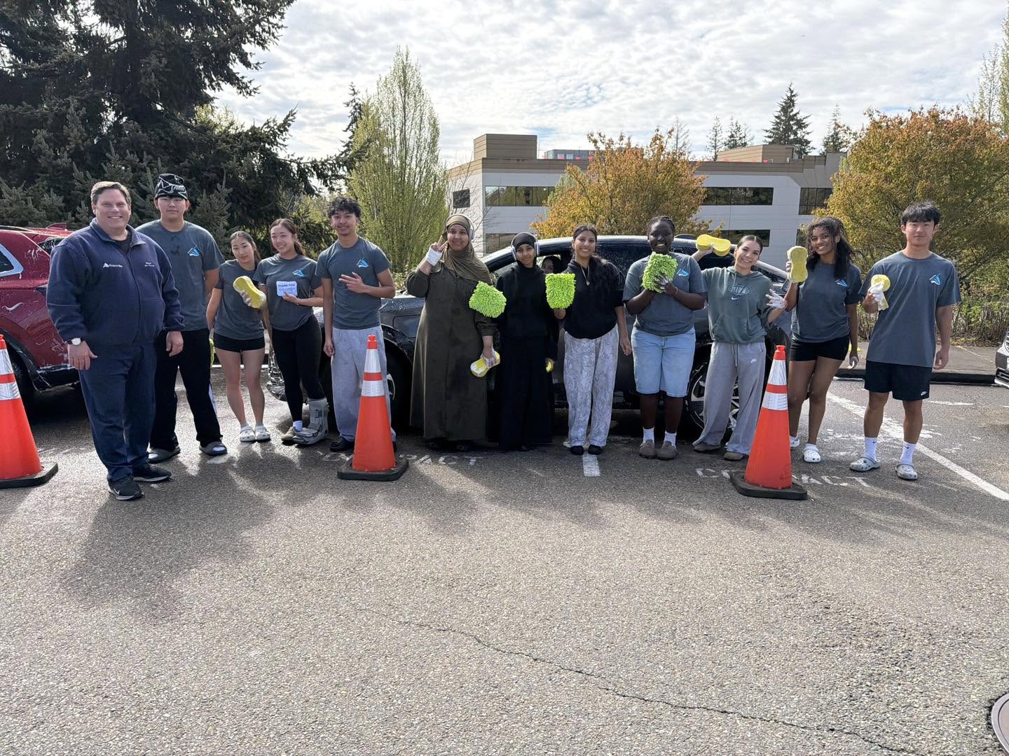 Youth Commission members and staff stand together outdoors in a parking lot, holding cleaning supplies and smiling for a group photo.
